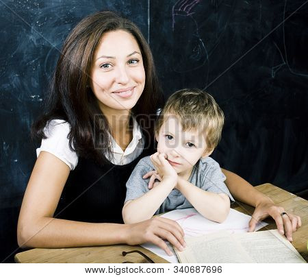 Little Cute Boy In Glasses With Young Real Teacher, Classroom Studying At Blackboard School Kido