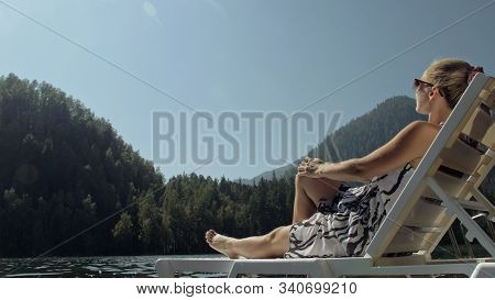 Woman Lie On A Sunbed In Sunglasses And A Boho Silk Shawl. Girl Rest On A Flood Wood Underwater Pier