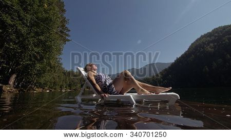 Woman Lie On A Sunbed In Sunglasses And A Boho Silk Shawl. Girl Rest On A Flood Wood Underwater Pier