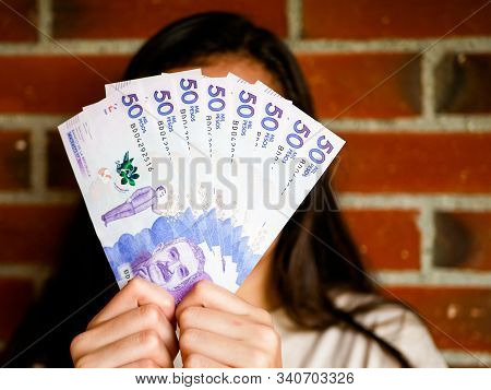 Woman Hiding Her Face With A Range Of Fifthy Tousand Pesos Bill And Bricks As A Backgound