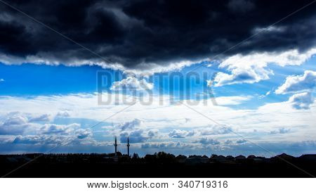 The Rays Of The Sun Breaking Through The Dark Evening Clouds. Silhouettes Of Two Mosque Minarets On 