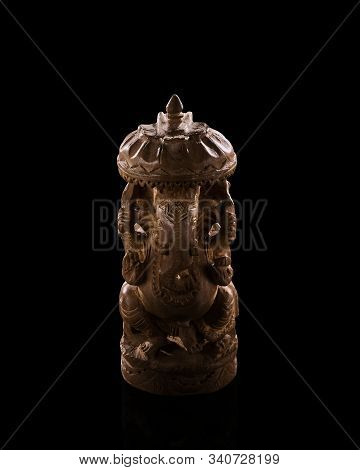 A Low Light Photo Of Indian God Ganesh Statuette. Figurine Made Of Sandalwood. Background Is Black, 