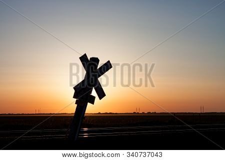 Railroad Crossing Sign On Prairie Silhouetted Against Sunrise Sky