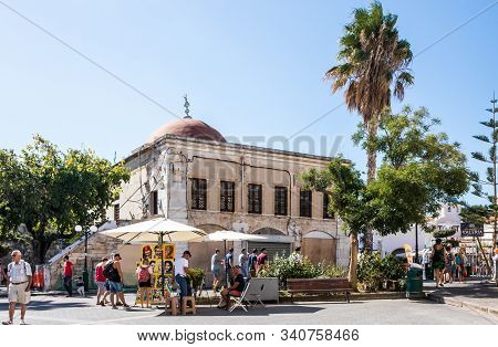 Kos, Greece - September 21st 2019: - People Walking Past Defterdar Mosque In Elefterias Square. This