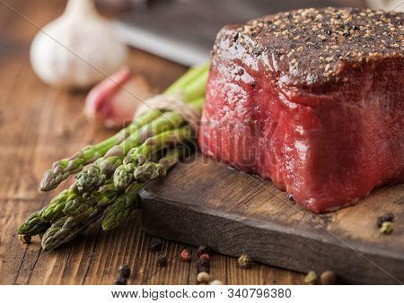 Slice Of Raw Beef Topside Joint With Salt And Pepper On Wooden Chopping Board With Garlic And Aspara