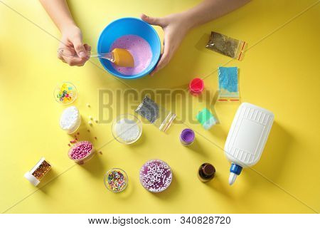 Little Girl Making Slime Toy On Yellow Background, Top View
