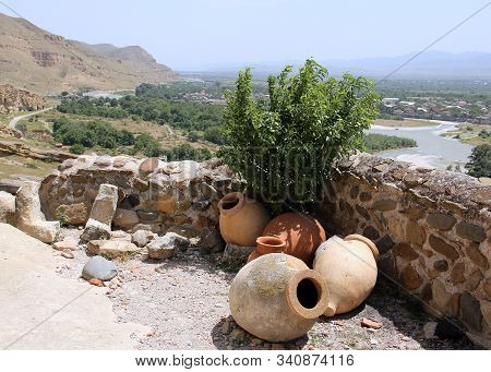 Gigantic Clay Wine Jugs Against The Stone Wall Of A Terrace Overlooking A River Valley, Georgia