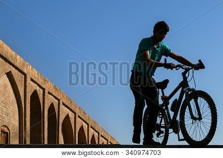 Iran, Isfahan, Khajoo Bridge - September 23, 2016: Young Guy With A Bicycle On The Old Bridge.