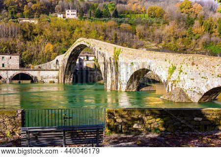 The bridge of Mary Magdalene is medieval structure that crosses the Serchio River. Italy, Lucca. The emerald cold water of the river reflects the ancient asymmetrical arches of the bridge