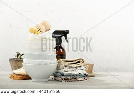 Zero waste home kitchen cleaning concept, front view of dishes, dish washing brushes, organic soap bar, kitchen towels, house plant and eco safe all purpose cleaner in reused glass jar