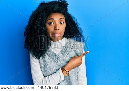 African american woman with afro hair wearing casual winter sweater pointing aside worried and nervous with forefinger, concerned and surprised expression 