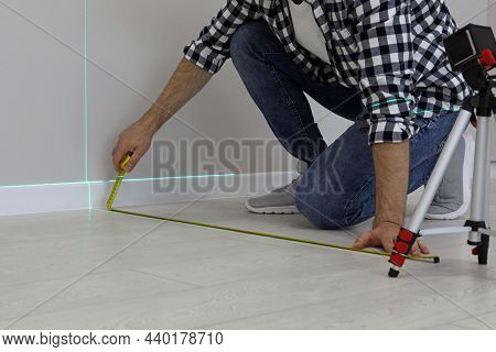 Man Using Cross Line Laser Level And Tape For Accurate Measurement On Floor, Closeup