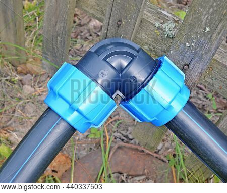 Fragment Of Low-pressure Aboveground Plastic Water Supply System Near  Blur Old Wooden Fence In Coun