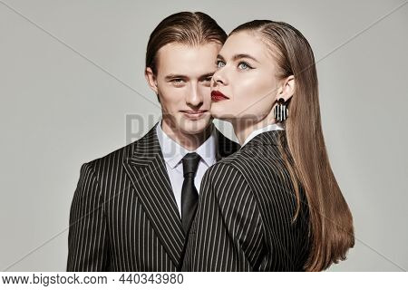 Beautiful young couple in smart striped pantsuits poses on a gray studio background. Impeccable look. Business style. Fashion shot. 