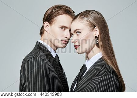 Impeccable look. Portrait of stylish young couple in smart striped pantsuits posing on a gray background. Business style. Fashion shot. 