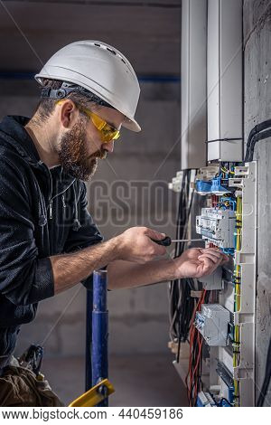 A Male Electrician Works In A Switchboard With An Electrical Connecting Cable.
