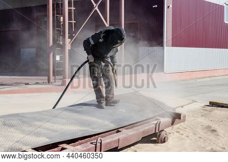 A Worker In A Special Suit Is Sandblasting Metal At An Industrial Site