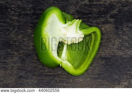 Half Of The Fresh Green Bell Pepper Cut Lengthwise Lies On The Dark Surface, Top View