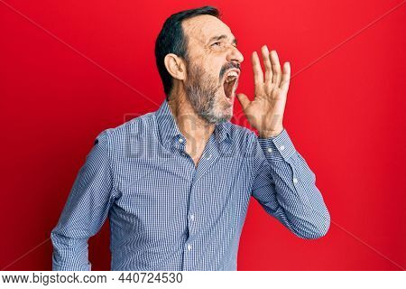 Middle age hispanic man wearing casual clothes shouting and screaming loud to side with hand on mouth. communication concept. 