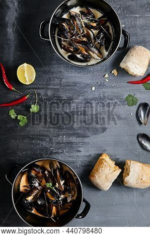 Mussel stew pot with creamy sauce, baguette on stone table. Mussels soup pot contemporary style. Aesthetic composition with seafood. Gastronomy mussel pot dinner concept. Stone table and wooden tray