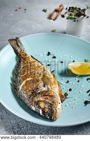 Grilled dorada in blue plate on stone background with textile. Roast fish in restaurant menu concept. Roasted whole dorado with lemon. Contemporary seafood menu. Mediterranean food