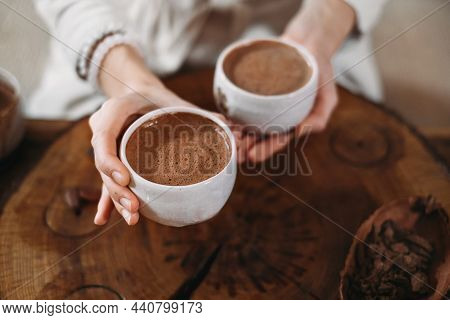 Hot Handmade Ceremonial Cacao In White Cups. Woman Hands Giving Craft Cocoa, Top View On Wooden Tabl