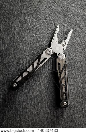 Multi-tools pliers with other tools and knife. Multifunction pliers on stone table. Top view.