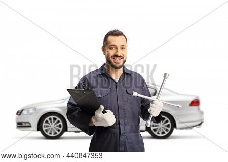 Auto mechanic worker holding a lug wrench in front of a silver car isolated on white background