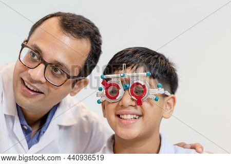 Smiling Indian Boy Choosing Glasses In Optics Store, Boy Doing Eye Test Checking Examination With Op