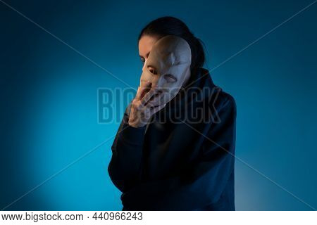 Hiding Behind A Mask, A Young Woman In A Dark Hoodie Hides Her Face With A Mask, The Concept Of Self