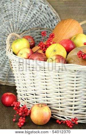 Juicy apples and pumpkin in wooden basket on table close-up