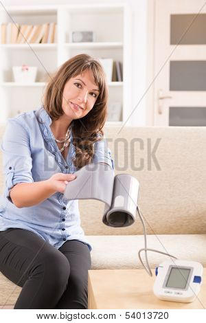 Beautiful woman checking her blood pressure at home and presenting pressure monitor cuff