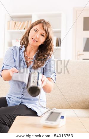 Beautiful woman checking her blood pressure at home and presenting pressure monitor cuff