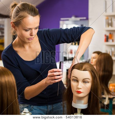 Pretty female hairdresser/haidressing apprentice/student training on an apprentice head