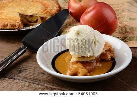 Closeup of a slice of Apple Pie a la Mode. Fresh Fuji apples and a whole pie are in the background. Horizontal format.
