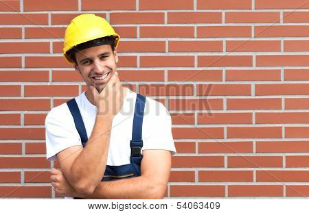 Thinking young worker in front of a brick wall