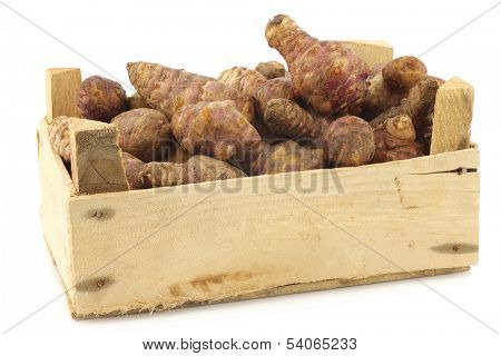 bunch of topinambur roots (helianthus tuberosus) in a wooden crate on a white background
