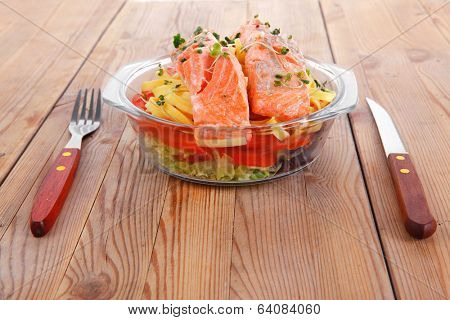fresh fried natural pink salmon on italian traditional tagliatelle backed with tomato and vegetables served over wooden table with cutlery