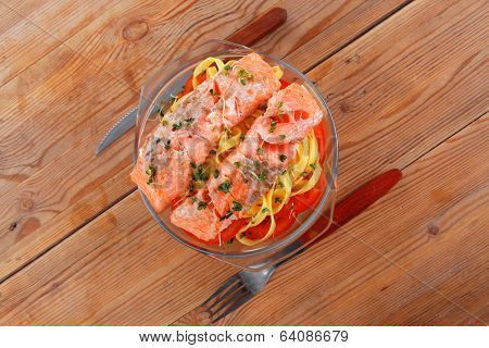 fresh fried natural pink salmon on italian traditional tagliatelle backed with tomato and vegetables served over wooden table with cutlery