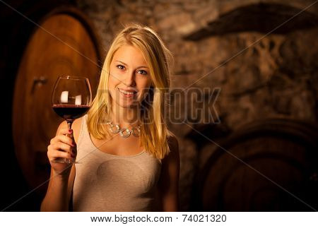 Beautiful Young Blond Woman Tasting Red Wine In A Wine Cellar
