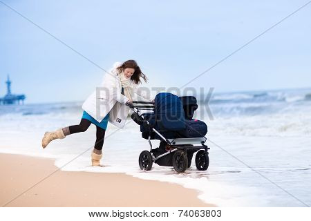Happy active young mother walking on a beach pushing an all terrain double stroller