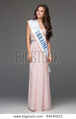 Beautiful young brunette woman with her hair posing in a i long dress. Studio, on gray background