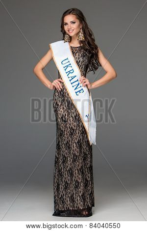 Beautiful young brunette woman with her hair posing in a i long dress. Studio, on gray background