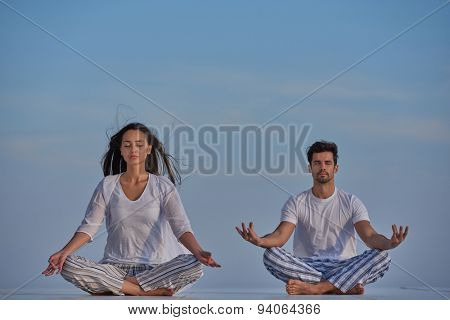 young couple practicing yoga at sunset in modern home terace with ocean and sunset in background