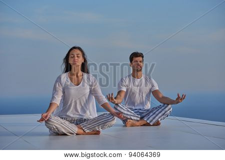 young couple practicing yoga at sunset in modern home terace with ocean and sunset in background