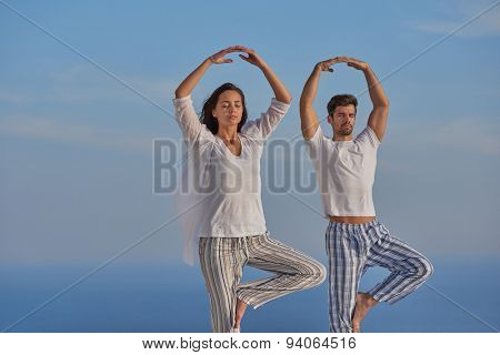 young couple practicing yoga at sunset in modern home terace with ocean and sunset in background