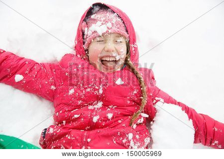 Playful girl with braids playing in snow throwing it in the air having fun enjoying and being active. Natural lifestyle and free childhood concept with copy space.