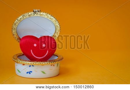 Jewelry box with a red smiley heart inside on yellow background