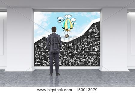 Rear view of man looking at blackboard with white business sketches and sky with hot air balloon in office lobby. Concept of no limits to perfection. 3d rendering. Mock up