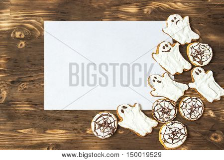 Funny delicious ginger homemade biscuits for Halloween on the dark wooden table with sheet of papper as a space for text. horizontal view from above. Halloween cookies